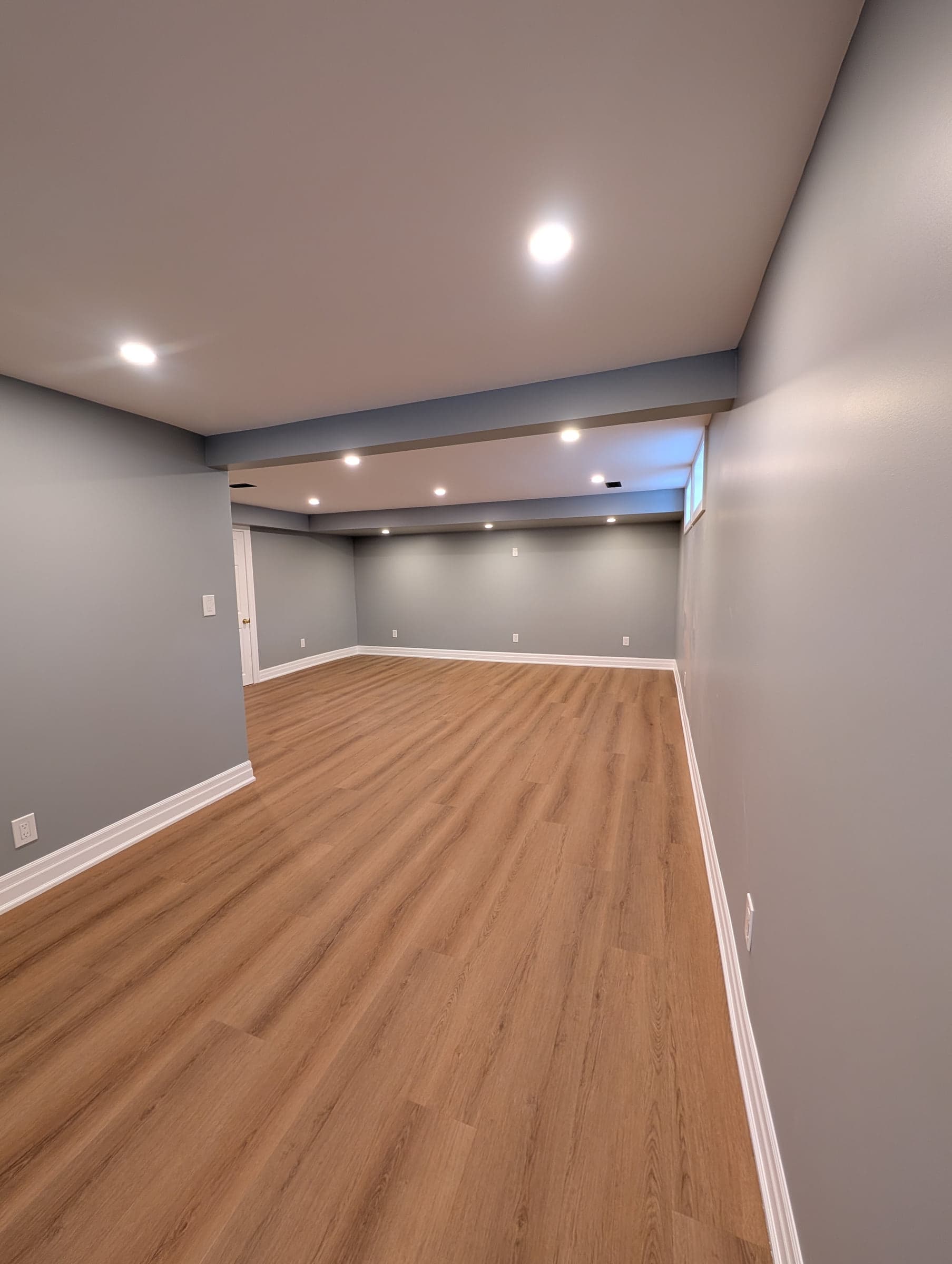 Finished empty basement room with light walls, flooring, and recessed lighting