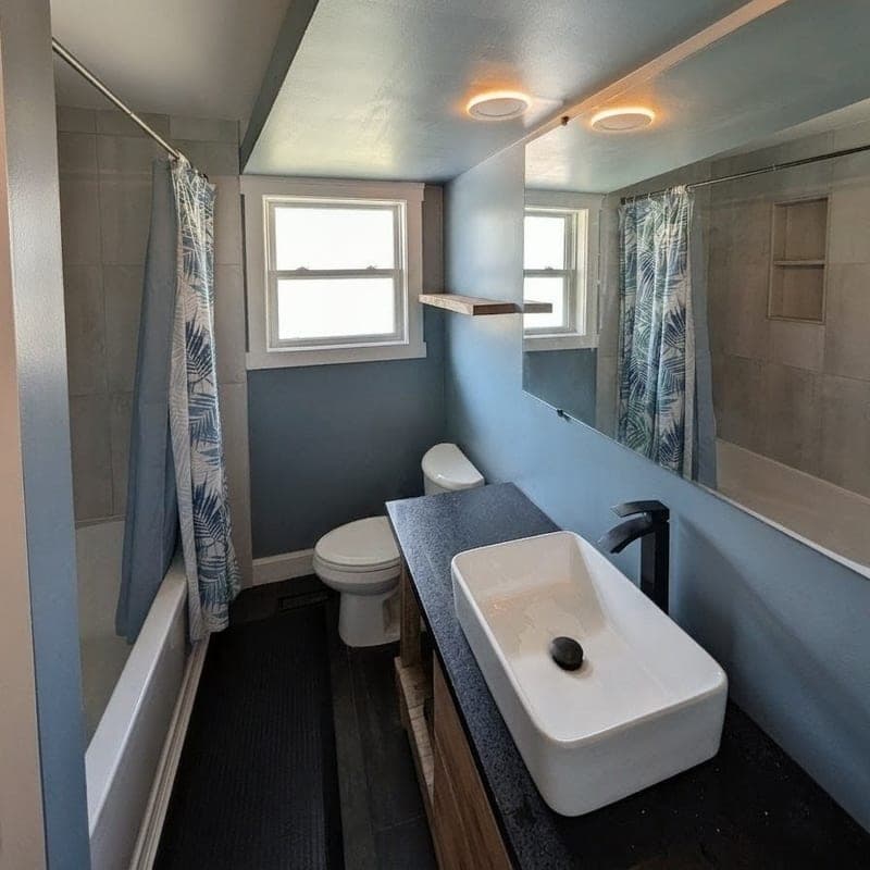 The same bathroom after renovation with a vessel sink and blue-grey walls