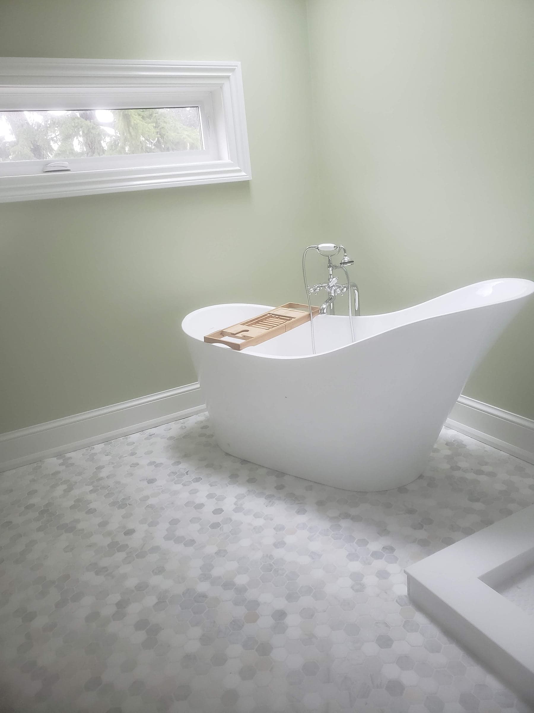 Freestanding bathtub beside a tiled wall and window