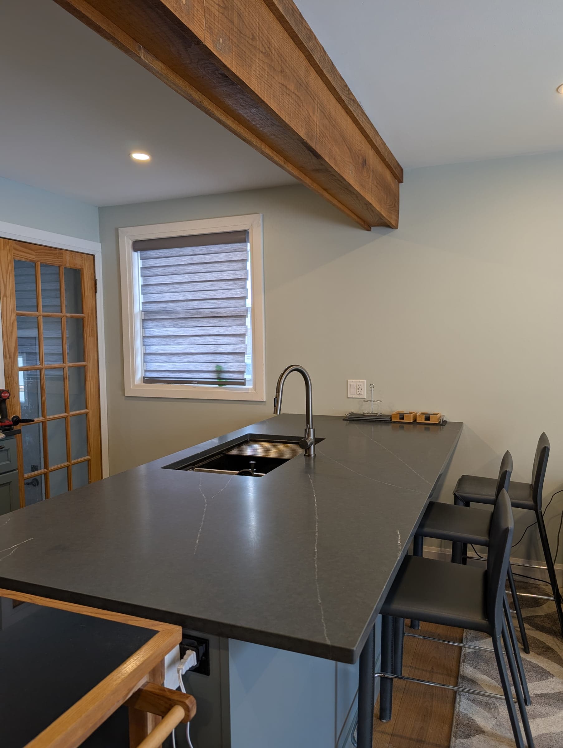 Long dark kitchen peninsula beneath a wood ceiling beam