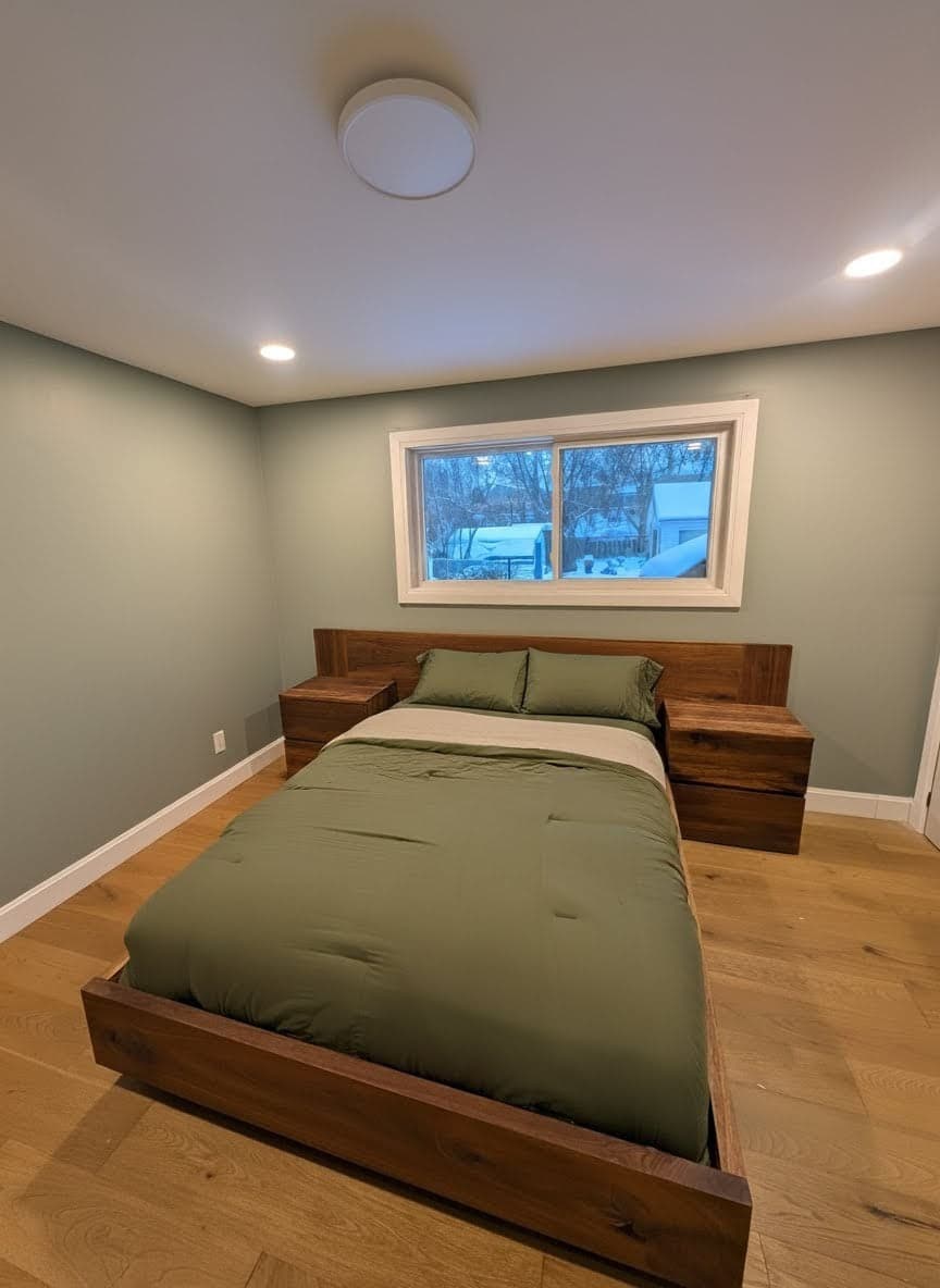 Finished bedroom with light walls, wood-look flooring, and a window