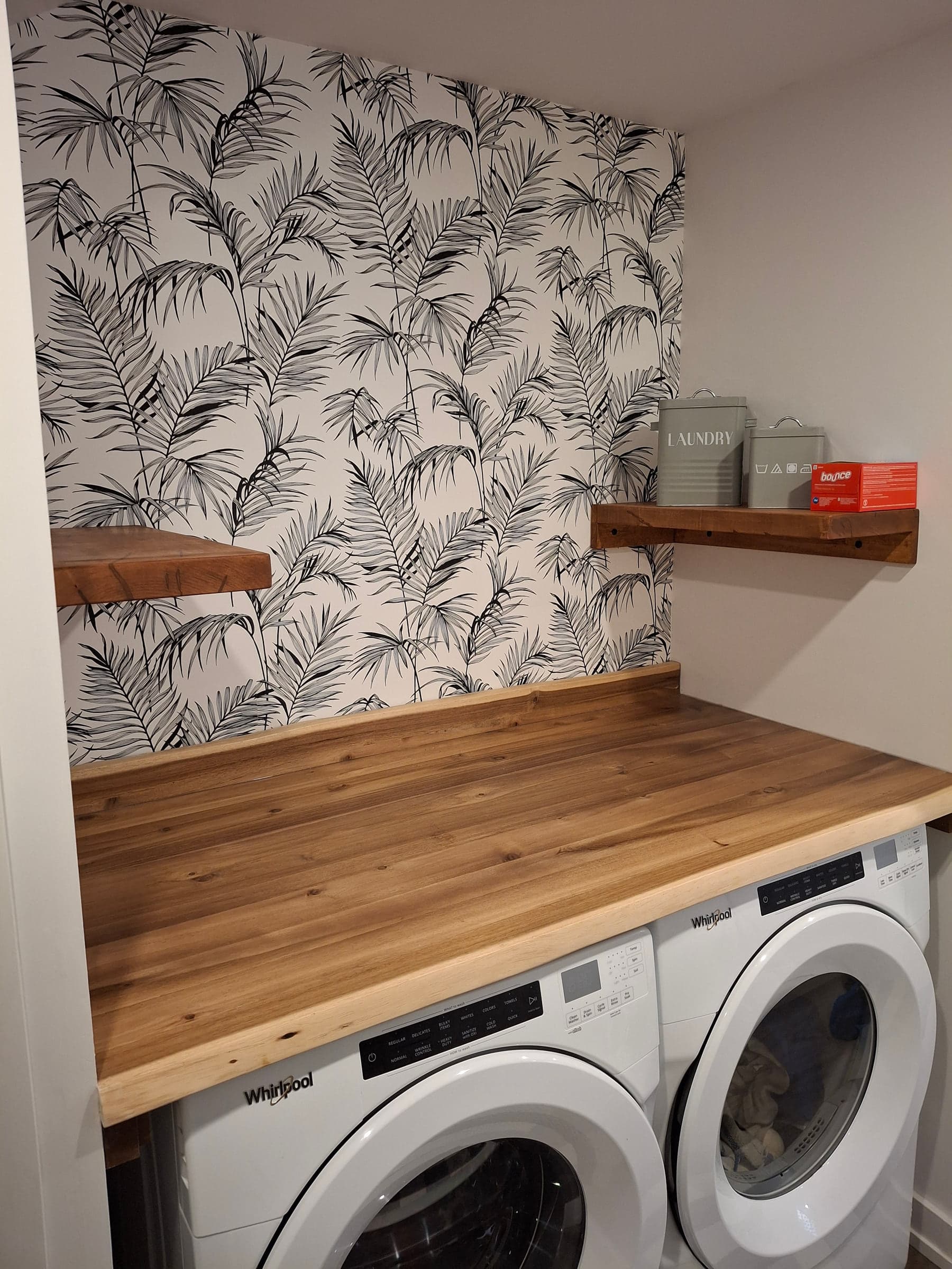 Laundry area with wood counter, patterned wall, and front-loading machines